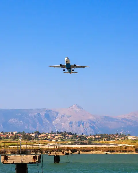 Avion care decolează pe cer senin deasupra mării și a munților din Corfu