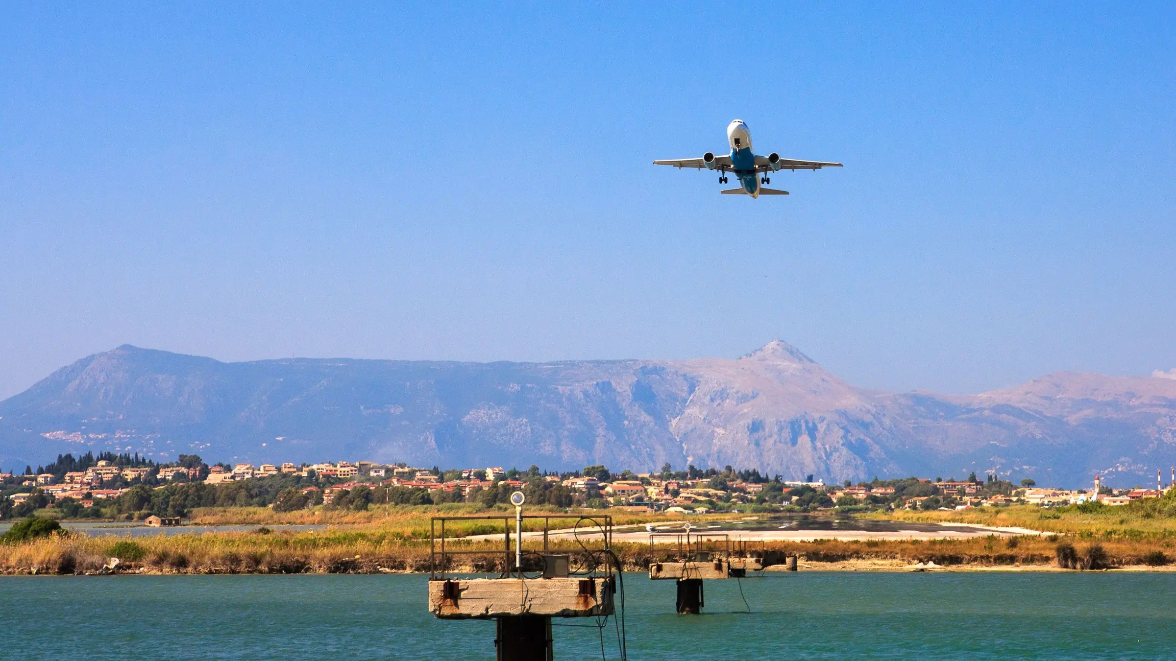 Avion care decolează pe cer senin deasupra mării și a munților din Corfu