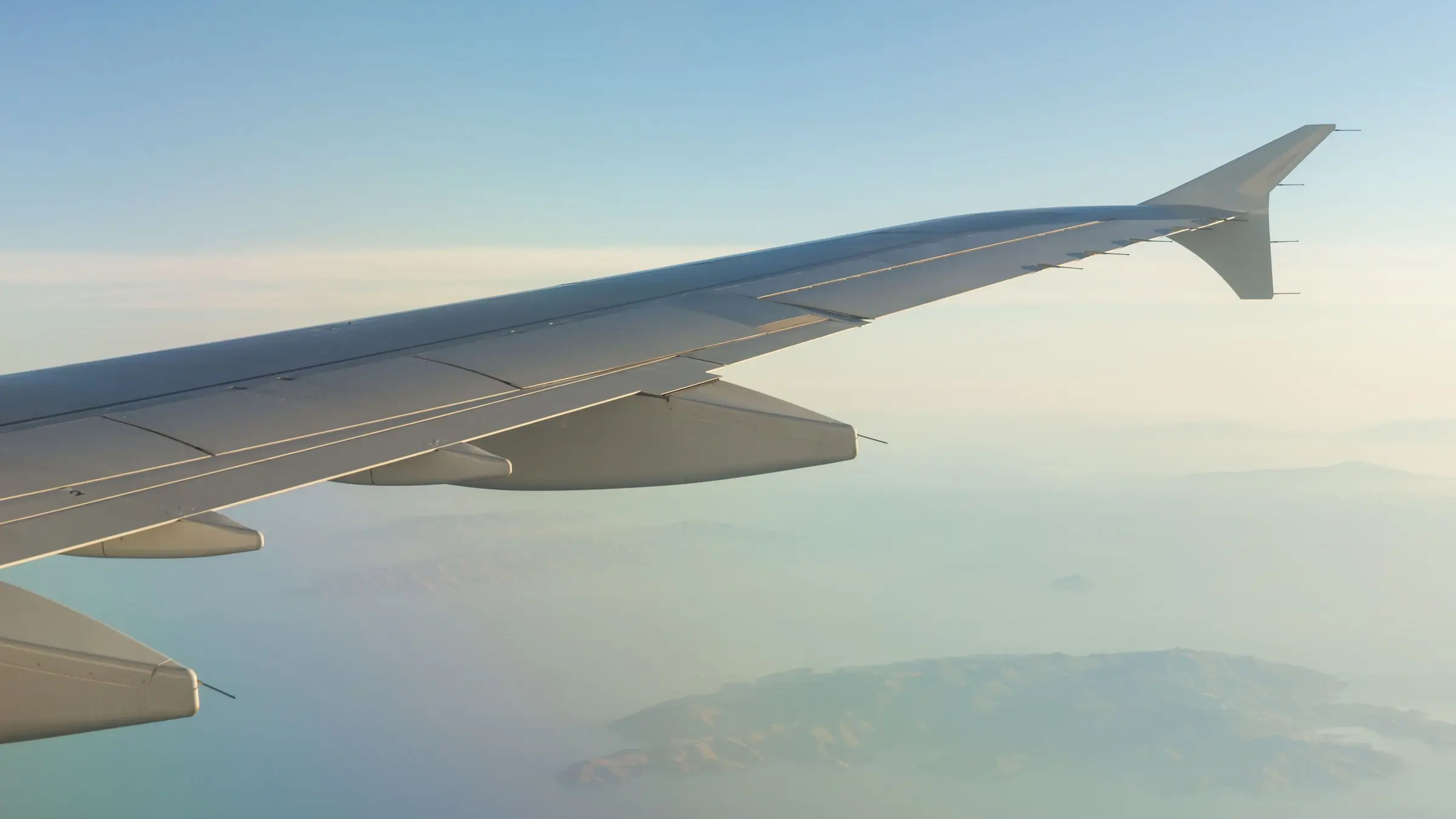 Aripa avionului deasupra mării și a unei insule, văzută prin hublou