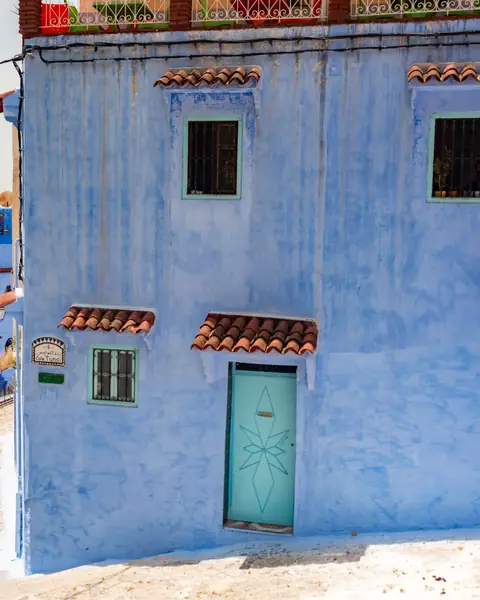 Casă albastră cu ușă turcoaz pe o stradă în pantă din Chefchaouen, Maroc
