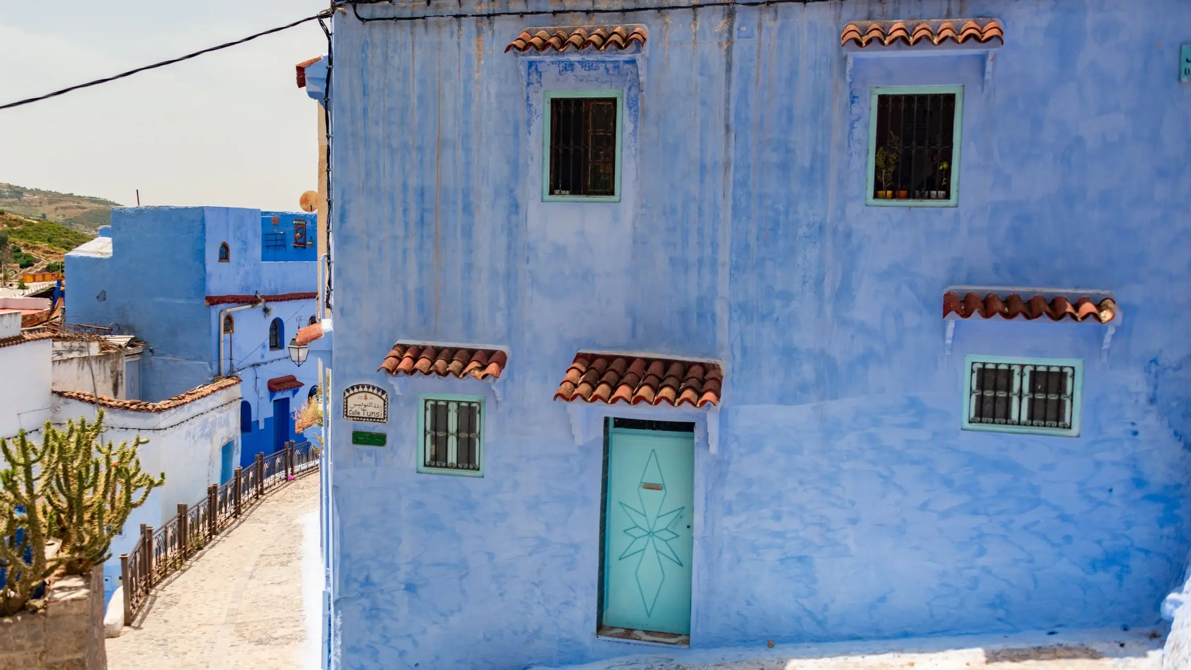 Casă albastră cu ușă turcoaz pe o stradă în pantă din Chefchaouen, Maroc