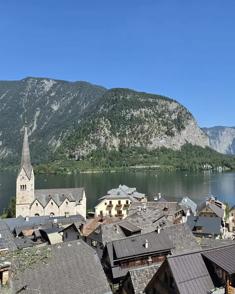 Satul Hallstatt cu turla bisericii, acoperișuri vechi și lacul între munți, sub cer senin