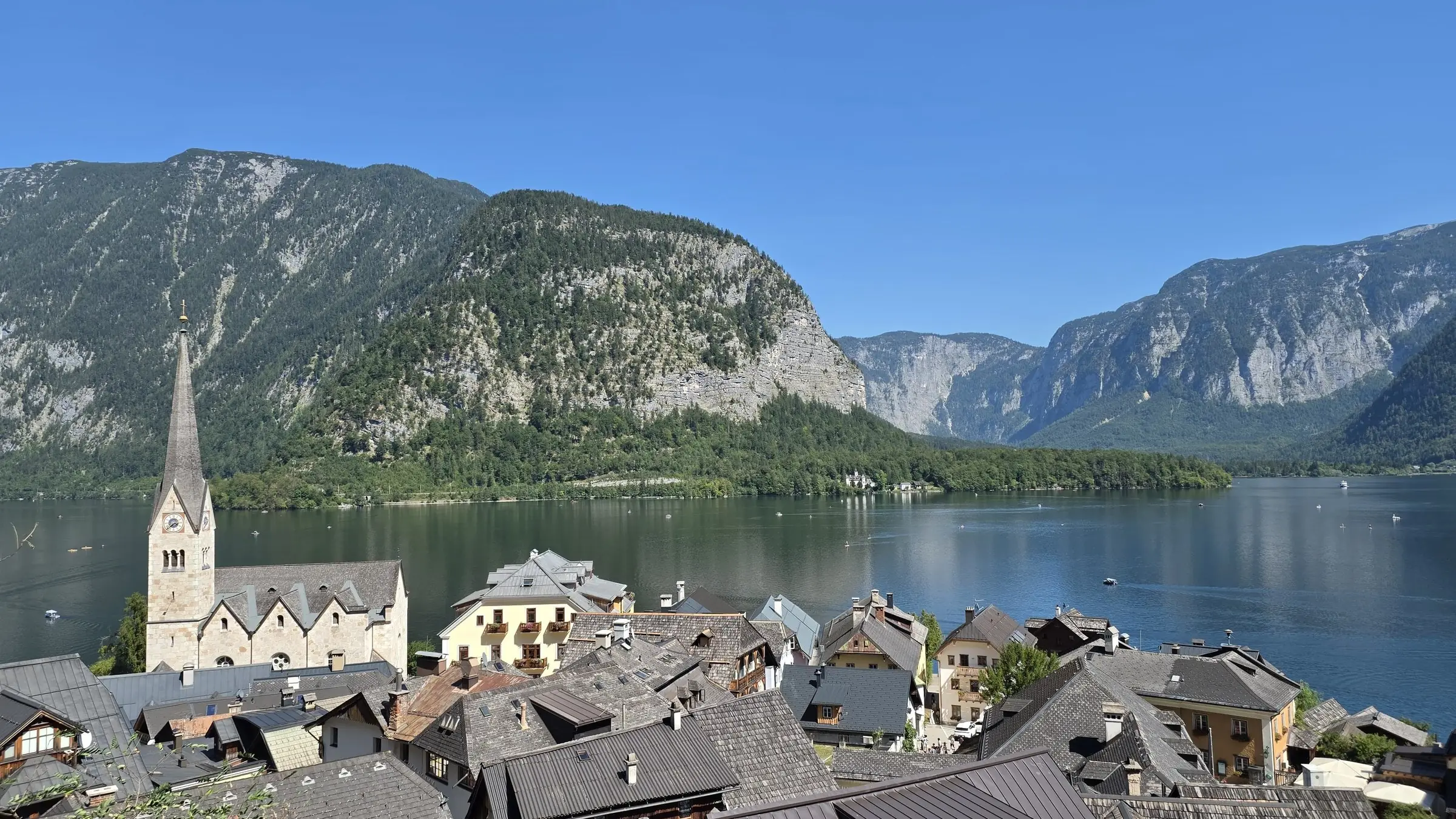 Satul Hallstatt cu turla bisericii, acoperișuri vechi și lacul între munți, sub cer senin