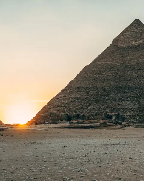 Piramidele de la Giza la apus, cu soarele între ele și cer auriu