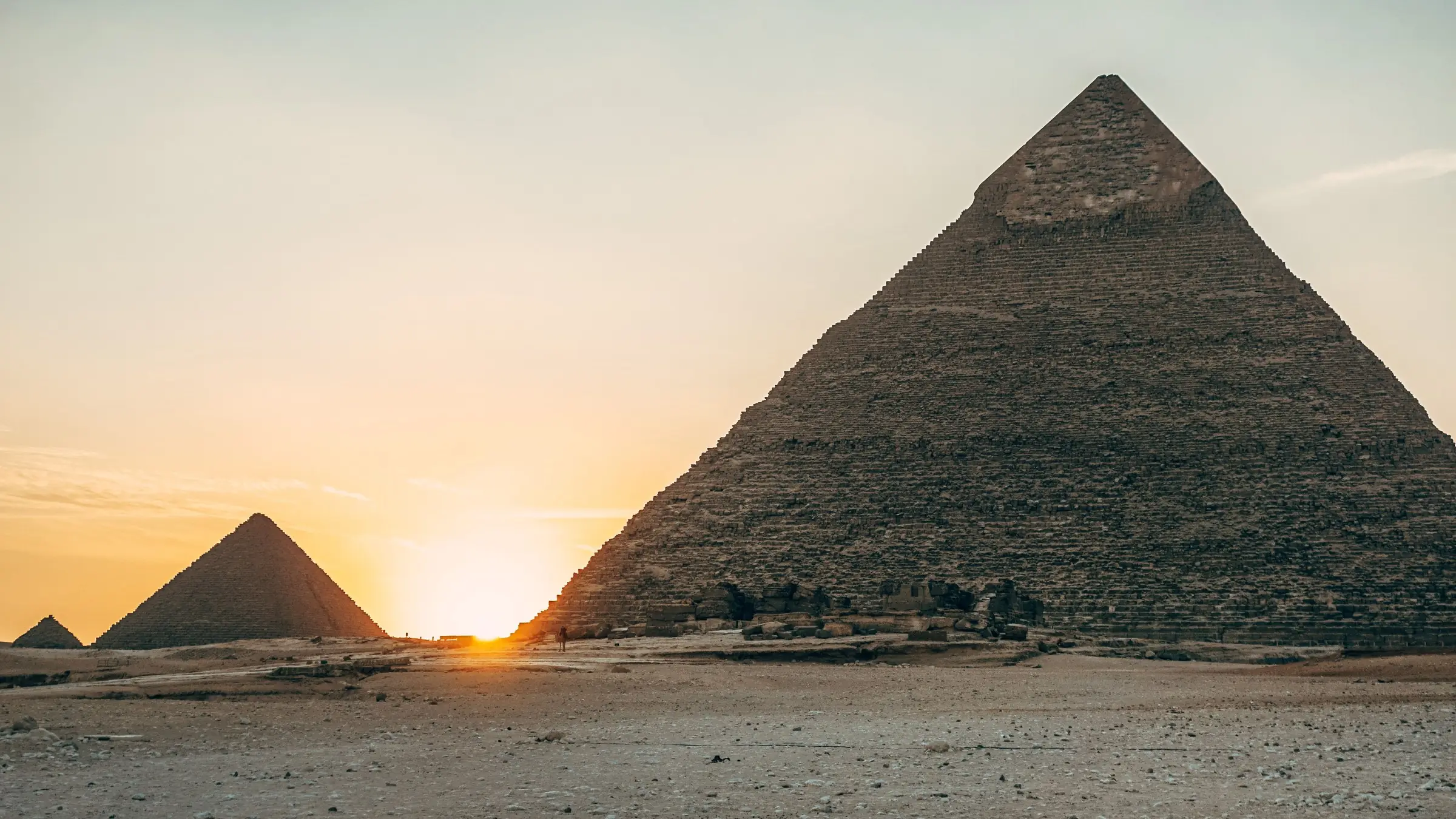 Piramidele de la Giza la apus, cu soarele între ele și cer auriu