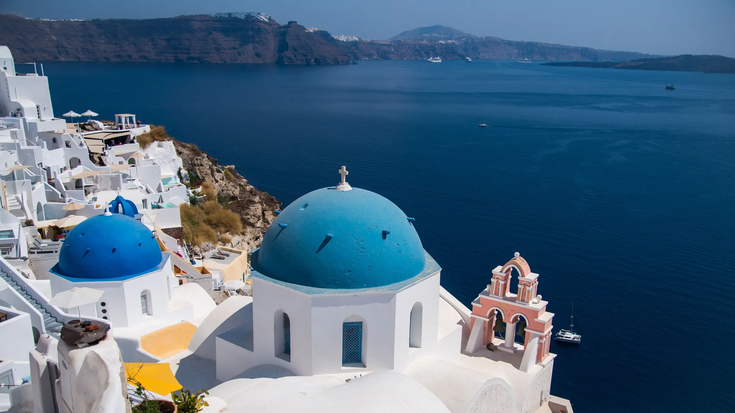 Cupole albastre și case albe în Oia, Santorini, deasupra calderei