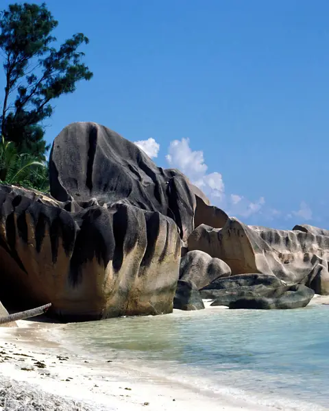 Bolovani de granit pe o plajă din La Digue, Seychelles, cu apă limpede și cer senin