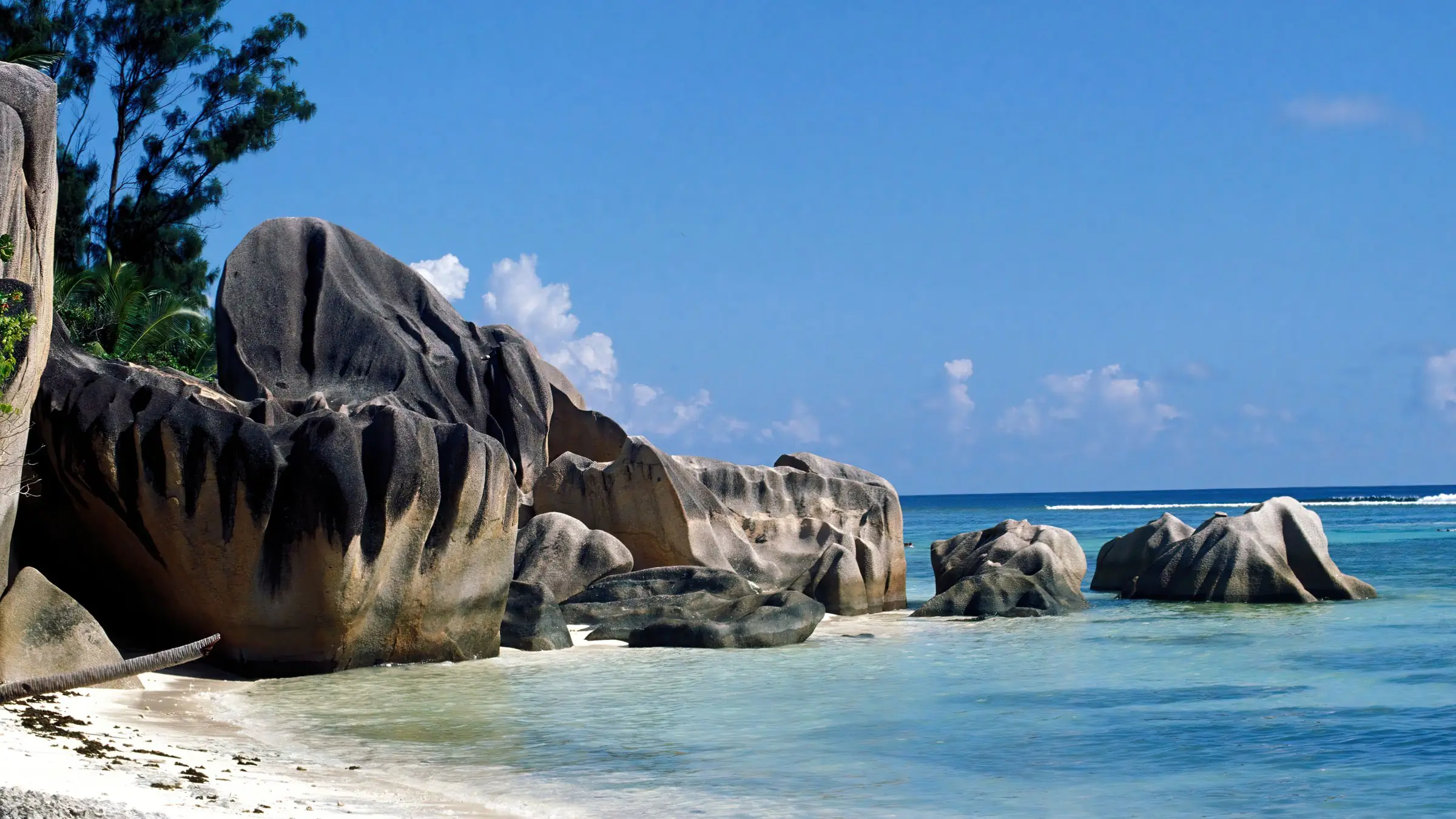 Bolovani de granit pe o plajă din La Digue, Seychelles, cu apă limpede și cer senin