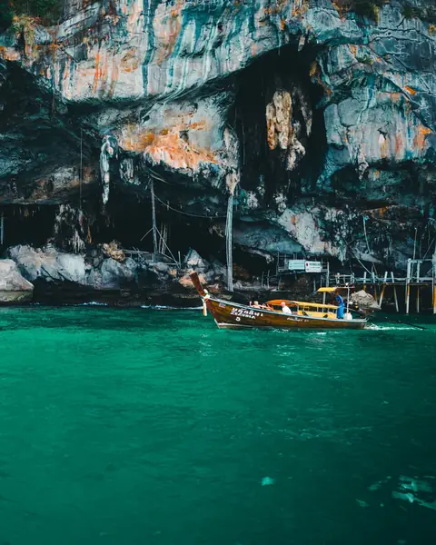 Barcă longtail tradițională lângă stâncile de calcar din Phuket, pe apă turcoaz