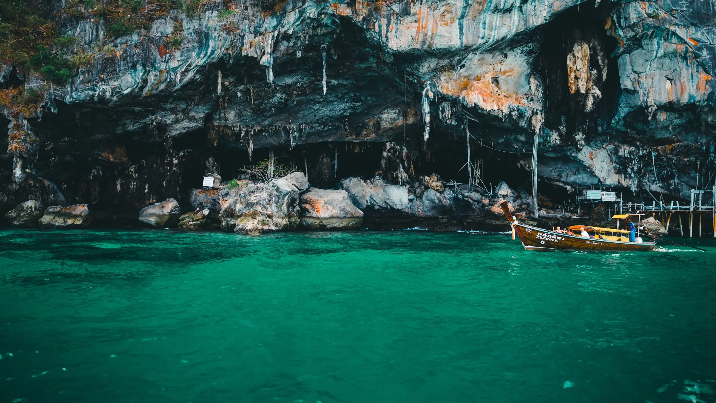 Barcă longtail tradițională lângă stâncile de calcar din Phuket, pe apă turcoaz