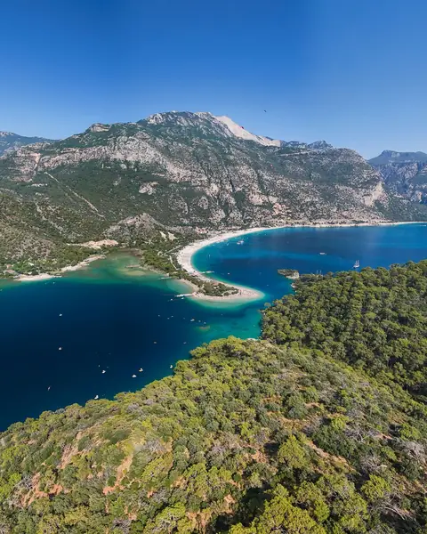 Laguna Albastră de la Ölüdeniz, cu plajă albă și munți împăduriți sub cer senin